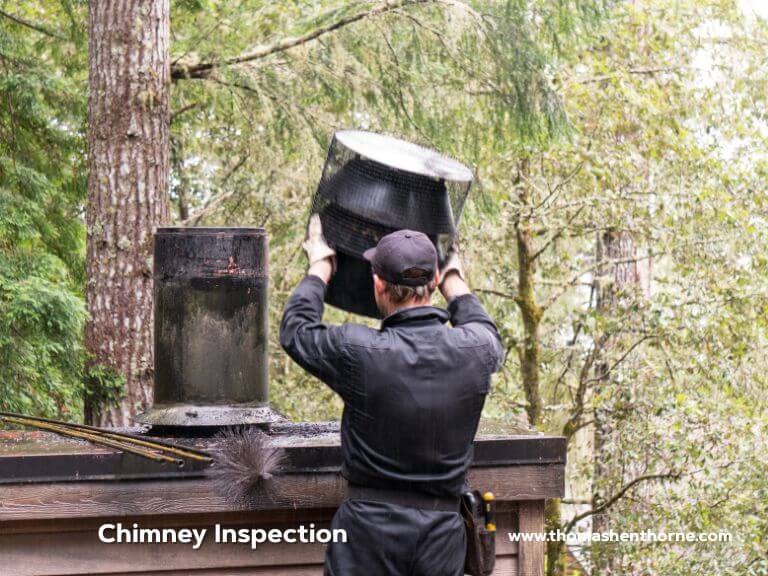 A worker dressed in black attire lifts a chimney cap atop a roof encircled by trees. The image includes the words Chimney Inspection and www.thorlasenthorn.com positioned in the bottom corners.