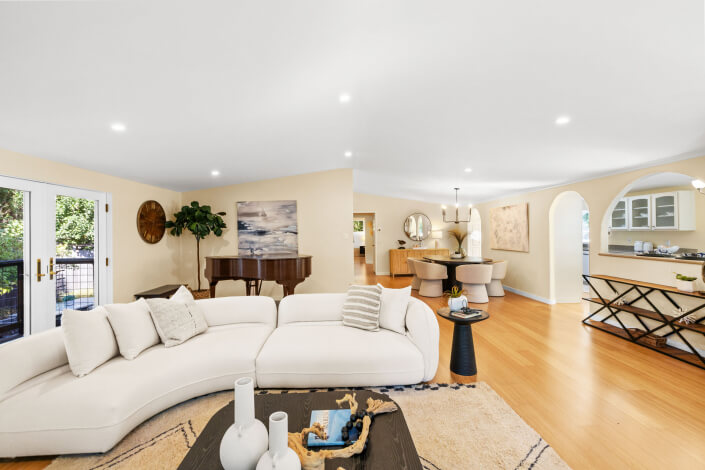 A spacious living room at 102 Clorinda Avenue Gerstle Park features light wood floors, cream walls, a curved white sofa, black piano, dining area with round table, large windows, and stylish accents in a bright, airy space.