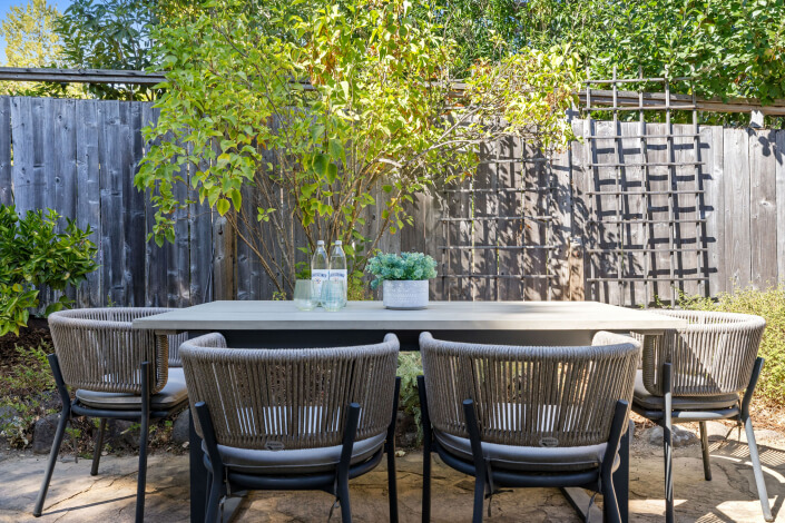 A table and chairs outside with a fence and trees in the background.