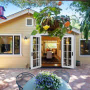 260 Clorinda Avenue San Rafael features open French doors to a sunlit living room. The patio offers a round table with potted flowers, hanging plants, and a red bird feeder—perfect for enjoying the welcoming outdoor space.