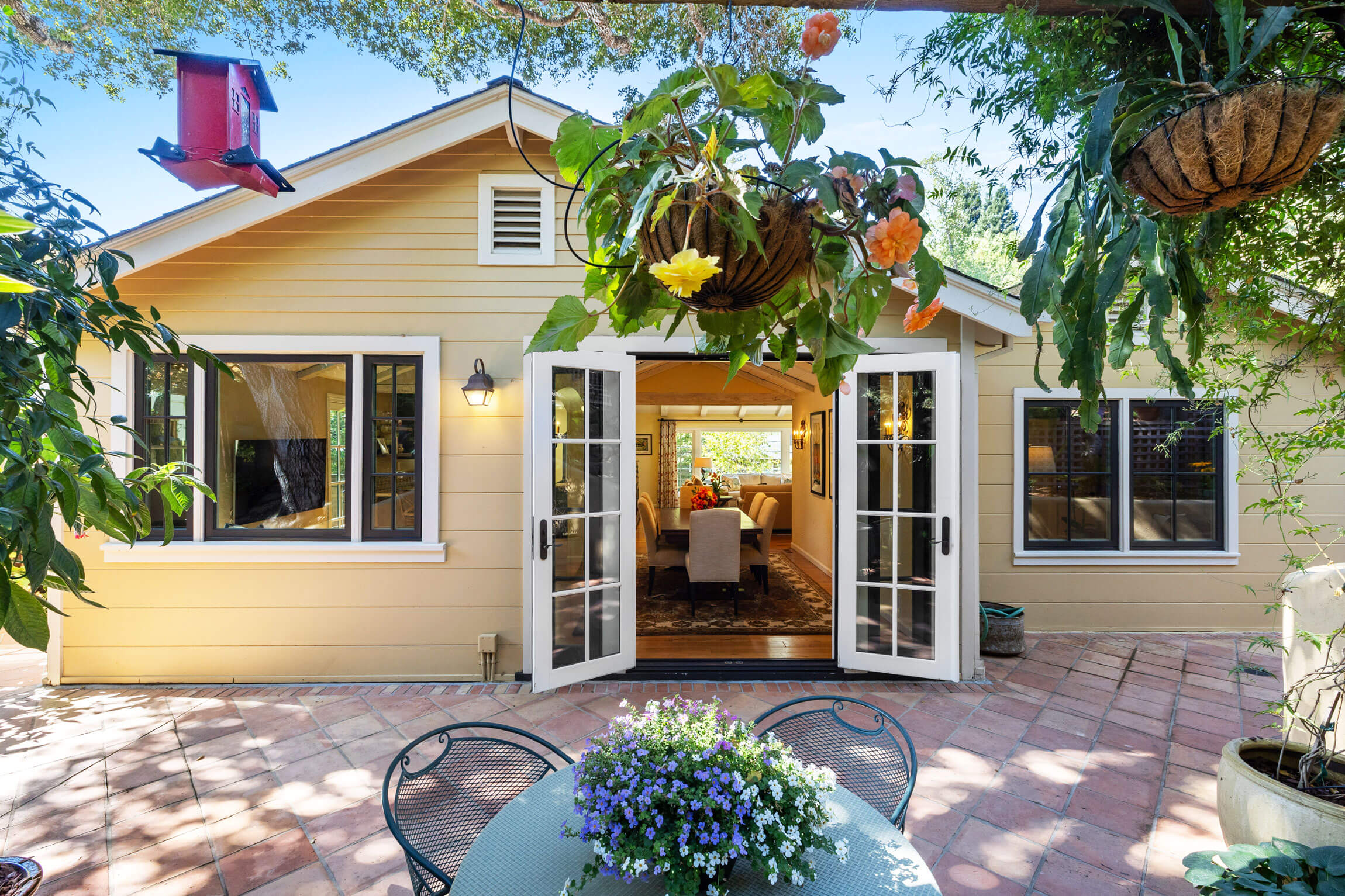 260 Clorinda Avenue San Rafael features open French doors to a sunlit living room. The patio offers a round table with potted flowers, hanging plants, and a red bird feeder—perfect for enjoying the welcoming outdoor space.
