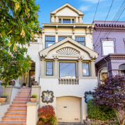 A two-story house at 739 10th Avenue, San Francisco, features large windows, decorative architectural details, a small garage, and a staircase leading to the entrance. Surrounded by trees and plants, it sits beside a purple neighboring building.