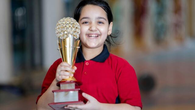 A girl wearing a red shirt holding a trophy.