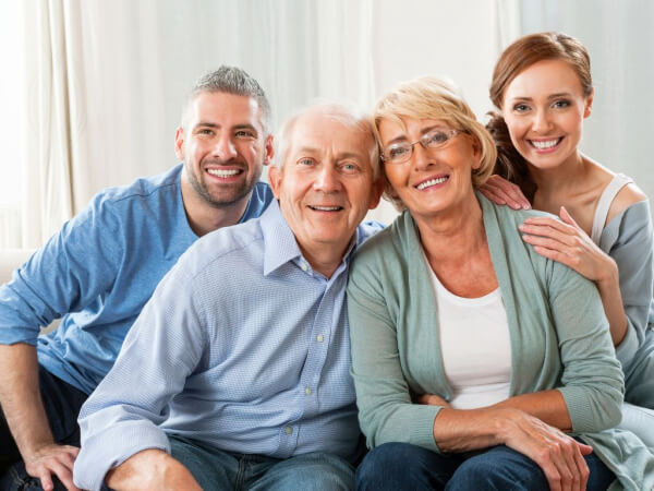Marin estate sales family first Two smiling older adults sit closely together on a couch, with a younger man and woman standing behind them, all looking at the camera in a bright, cozy indoor setting.