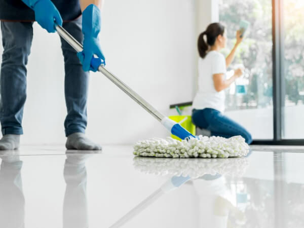 marin estate sales final cleanout of home Person wearing blue gloves mops a shiny white floor, while another person cleans a glass door in the background. Both are engaged in house cleaning tasks.