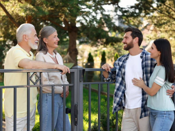 marin estate sales talk to your neighbors Two older adults and two younger adults stand and smile at each other while chatting over a metal fence outdoors, with green trees and sunlight in the background.