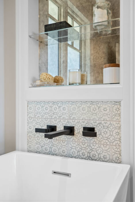 Close-up of a modern bathroom sink featuring a sleek black wall-mounted faucet and patterned tile backsplash. Above the sink, a recessed shelf displays decorative items, all bathed in natural light streaming from a nearby window.