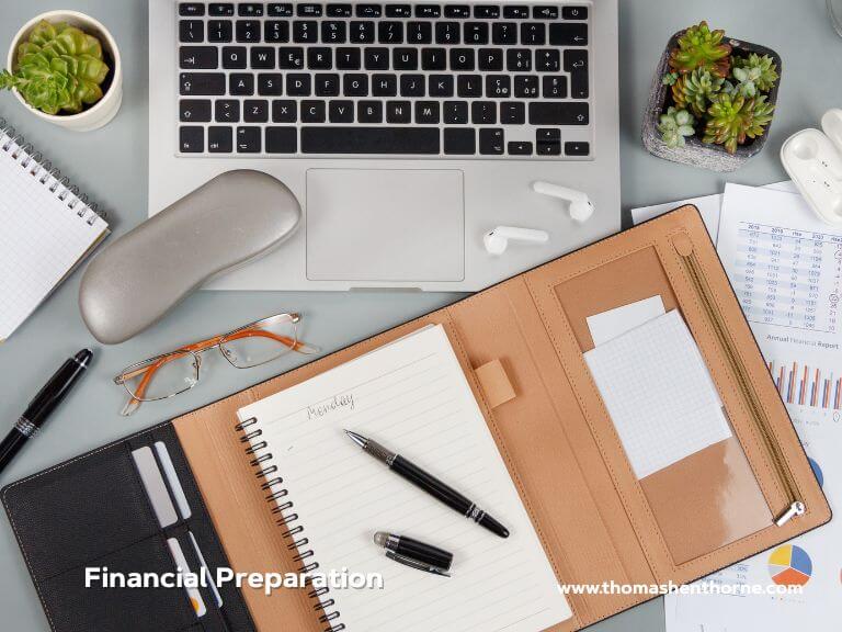 financial preparation design canva A workspace featuring a laptop, notebook, planner, pens, glasses, earphones, small succulents, and printed financial charts is arranged neatly. The image displays the text Financial Preparation and www.thomasenthorn.com.