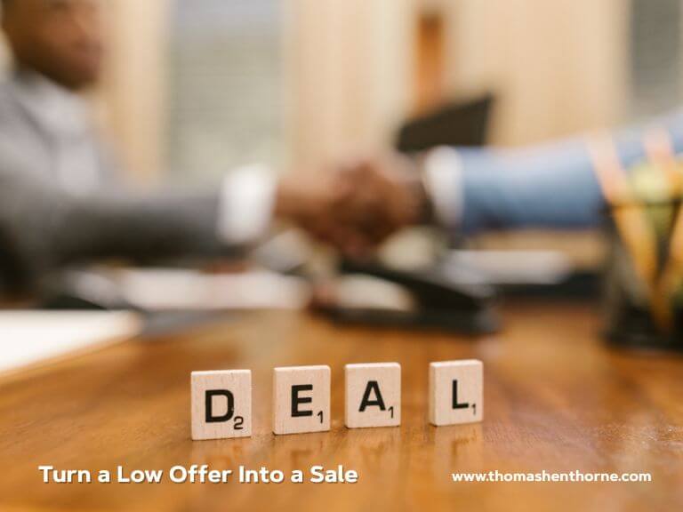 Scrabble tiles arranged to spell DEAL sit on a desk, while two people shake hands in the out-of-focus background. The image displays the text, "Turn a Low Offer Into a Sale," along with a visible website URL.